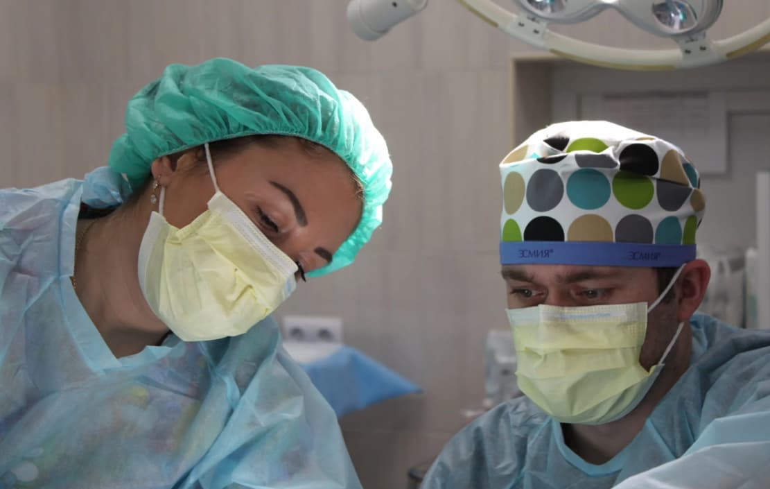 Two surgeons in scrubs and surgical caps, wearing masks in an operating room