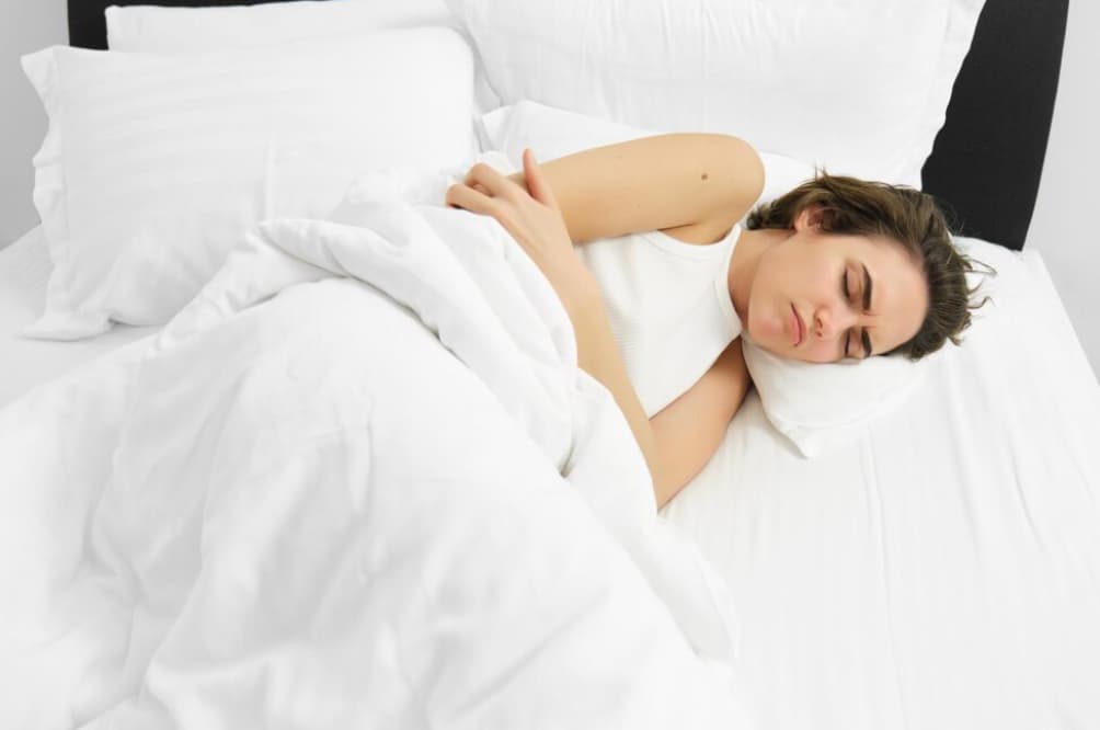 Woman lying in bed clutching her stomach in discomfort