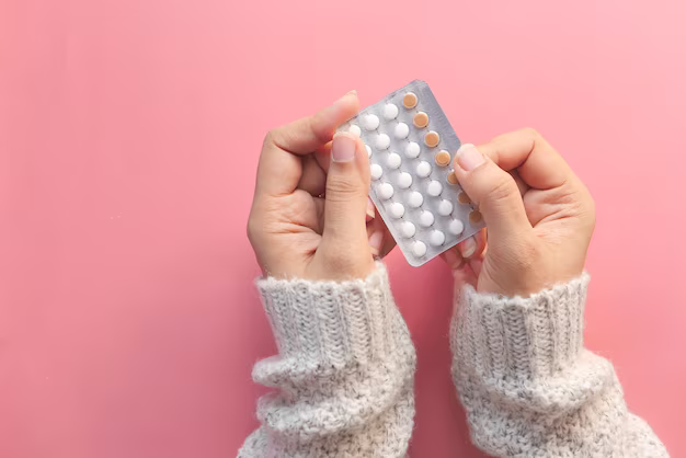 Hands holding birth control pills on pink background